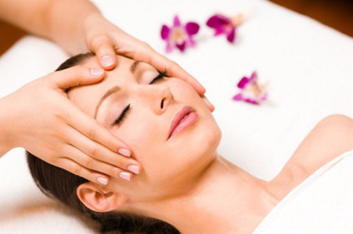Reiki nach Mikao Usui Frau erhält entspannende Gesichtsbehandlung mit Blumen im Hintergrund.