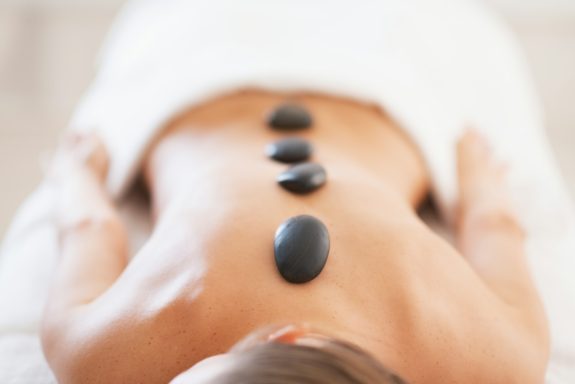 Hot Stone Massage mit Edelsteinen Glückliche Person mit heißen Steinen auf dem Rücken, entspannende Wellness-Anwendung.
